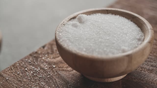 وعاء صغير من السكر الأبيض على طاولة خشبية
